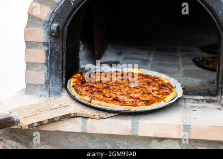 Pizza aus einem weiß lackierten, handgefertigten Holzofen, der auf der Außenseite gebaut wurde Stockfoto