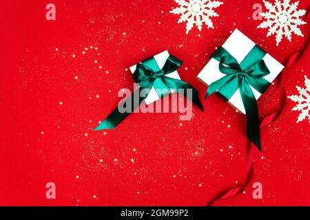 Große und kleine weiße Geschenkboxen mit einem grünen Satinband auf rotem Hintergrund gebunden. Schneeflocken, Sterne und Schneeflocken auf Papierhintergrund. Weihnachten A Stockfoto