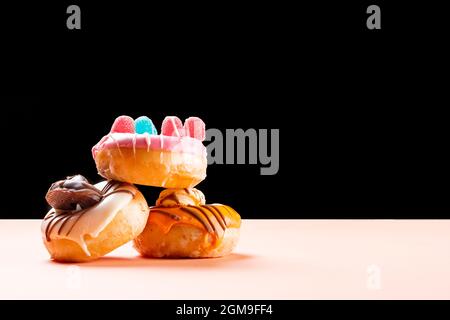 Foto von 3 Donuts mit Jelly Beans verziert und mit Schokolade gezeichnet.das Foto ist im horizontalen Format auf einem cremefarbenen Karton und einem aufgenommen Stockfoto