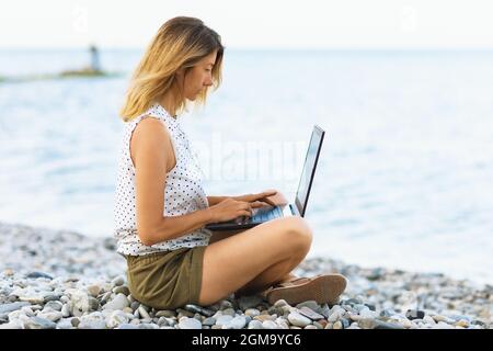 Eine Frau arbeitet an einem Computer am Meer, verbindet Ruhe und Arbeit Stockfoto