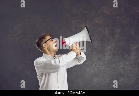 Seriöse junge kaukasische männliche Aktivistin gibt laut über Lautsprecher eine Ansage ab. Stockfoto