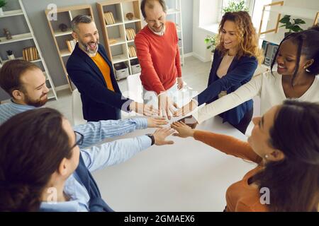 Fröhliche, multiethnische Volksgruppe schließen sich im Büro den helfenden Händen im Kreis an Stockfoto