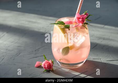 Frischegetränk oder Limonade mit Zitrone und Rosen mit sonnigem Schatten auf grauem Hintergrund. Nahaufnahme. Stockfoto