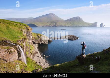 Der Typ macht Fotos am Telefon Skardsafossur Wasserfall und Drangarnir Meer Stapel Blick auf Färöer-Inseln Stockfoto