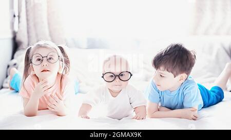 Kinder liegen auf dem Bett neben dem neugeborenen Baby, kleine Schwester. Die Emotionen von Kindern. Stockfoto