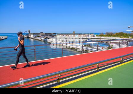 Oudor grüner und roter Teppich, Radweg und Fußweg, eine Frau geht auf einem Fußweg entlang einer Brücke auf einem Fluss in der Nähe des Meeres und am Strand Stockfoto