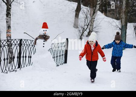 Kinder im Park im Winter. Kinder spielen mit Schnee auf dem Spielplatz. Sie Formen Schneemänner und rutschen Hügel hinunter. Stockfoto