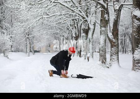 Ein Mann auf einem Spaziergang im Park. Junger Mann mit Regenschirm unter dem Winterschnee. Stockfoto