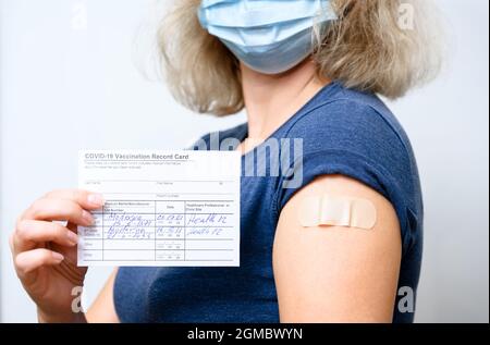 Geimpfte junge Frau in Maske mit COVID-19-Impfprotokollkarte, gesunde Person mit Gips am Arm nach Erhalt des Corona-Virus-Impfstoffs. Concep Stockfoto