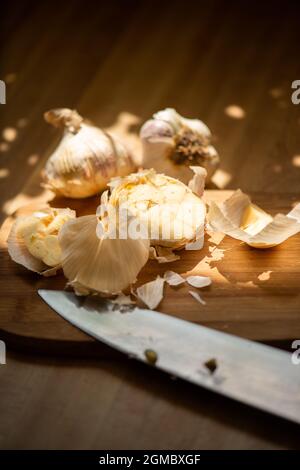 Mehrere Knoblauchzwiebeln auf Schneidebrett mit Küchenmesser im Vordergrund. Stockfoto