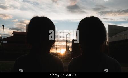 Zwei Geschwisterschwestern essen bei Sonnenuntergang süßes, leckeres Eis im Freien. Zwei glückliche junge Kinder genießen Dessert während der Ferien im Park. Stockfoto