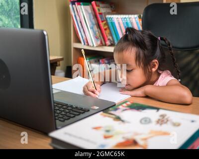 Nettes kleines Schulmädchen, das während ihres Online-Unterrichts zu Hause Hausaufgaben Mathematik studiert, soziale Distanzierung während des Coronavirus-Ausbruchs. Konzept von Online e Stockfoto