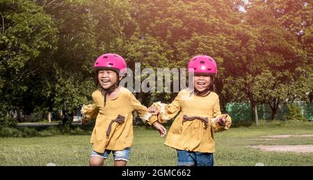 Zwei niedliche kleine Schwestern im Helm laufen an einem sonnigen Sommertag auf dem Rasen im Park und machen nach dem Radtraining eine Pause. Frohe Kindheit. Familie sp Stockfoto