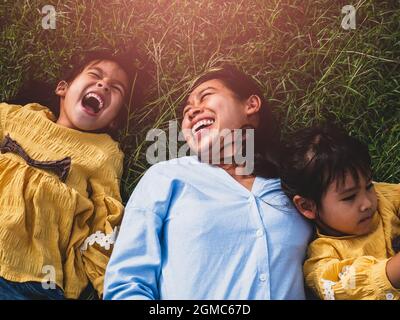 Glückliche Mutter und Töchter lächeln und lachen auf dem Rasen im Sommerpark liegen. Die Familie verbringt ihre Freizeit zusammen im Urlaub. Stockfoto