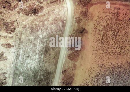 Unbefestigte Straße, die sich durch eine Buschlandschaft des Landes schlenderte, hochperspektivische Drohnenantenne, koloriertes Bild Stockfoto