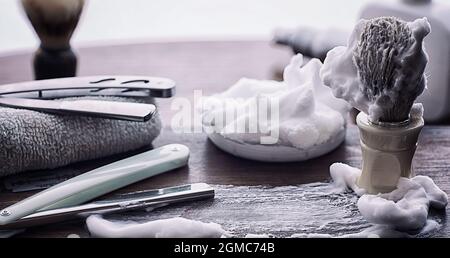 Rasierzubehör auf einem Hintergrund mit Holzstruktur. Werkzeuge. Einweg-Rasierer, Bürste, Rasierer mit Schaumgefahr. Stockfoto