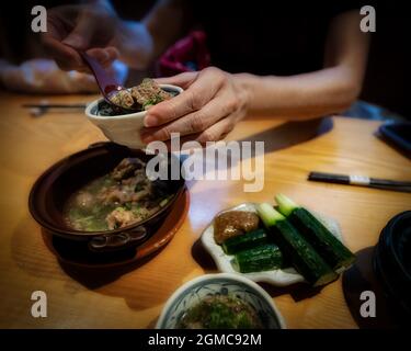Eine Dame schaufeln Fleisch und Brühe aus einer Schüssel an einem Tisch in Osaka, Japan. Stockfoto