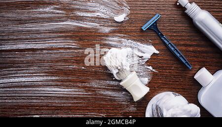 Rasierzubehör auf einem Hintergrund mit Holzstruktur. Werkzeuge. Einweg-Rasierer, Bürste, Rasierer mit Schaumgefahr. Stockfoto
