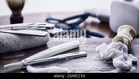 Rasierzubehör auf einem Hintergrund mit Holzstruktur. Werkzeuge. Einweg-Rasierer, Bürste, Rasierer mit Schaumgefahr. Stockfoto