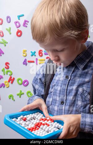 Vorderansicht eines intelligenten Jungen, der Abakus an einer grünen Tafel in einem Klassenzimmer der Grundschule hält Stockfoto