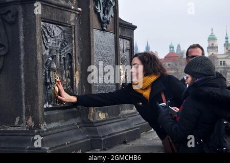 Die Frau, die die Gedenktafel unter der Statue des Hl. Johannes von Nepomuk berührt, soll Glück bringen und Ihre Rückkehr nach Prag auf der Karlsbrücke in Pra sicherstellen Stockfoto