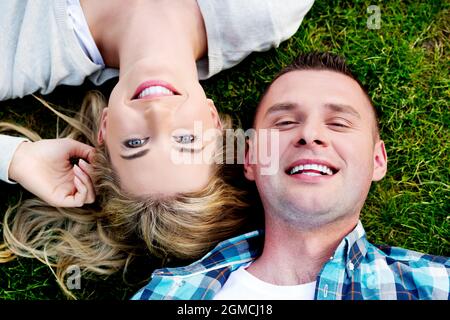 Draufsicht auf ein fröhliches polnisches Paar, das auf dem Rasen im Park liegt Stockfoto