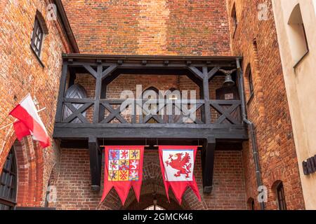 Blick auf die Mauern der gotischen Burg in Darłowo. Rote Ziegel und rote Fliesen bilden die Architektur der Burg. Fahnen und Holzbalkon Stockfoto