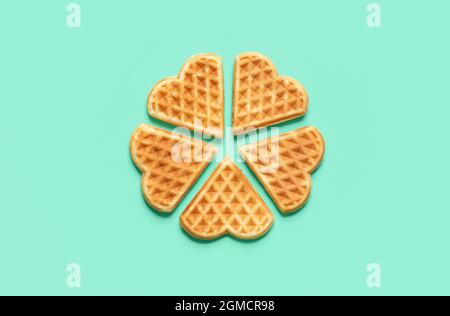 Oben mit herzförmiger Isolierung auf grünem Minzgrund. Hausgemachte belgische Waffeln, die im Kreis auf einem grünen Tisch angeordnet sind. Stockfoto