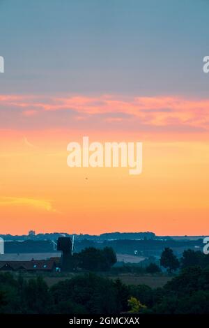 Ehemalige Windmühle in der Landschaft am Horizont in der Morgendämmerung am frühen Morgen das richtige Licht. Ein enges Band aus orange-rotem Himmel mit einer dicken Decke aus dunklen Wolken darüber. Stockfoto