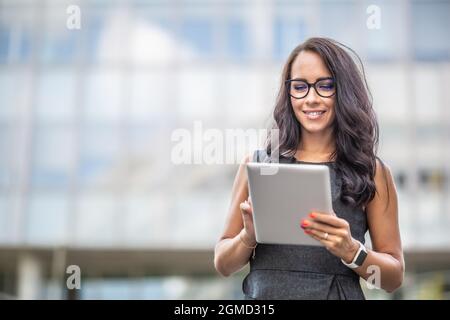 Eine gut aussehende Unternehmerin liest lächelnd von einem Tablet, das im Freien läuft. Stockfoto