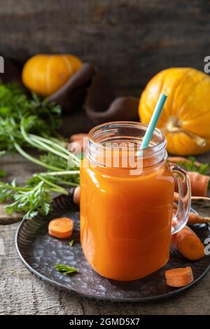 Frischer natürlicher Mischsaft, gesundes Lebensmittelkonzept. Glas mit frischem Karottensaft mit frischen Karotten und Kürbis auf einem rustikalen Holztisch. Speicherplatz kopieren. Stockfoto
