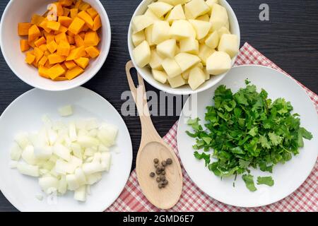 Zutaten für Suppe, Draufsicht auf Karotte, Zwiebel, Kartoffel, Koriander, Pfeffer in weißen Keramikplatten, Gemüseset Stockfoto