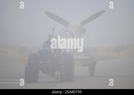 IWM Duxford, Cambridgeshire, Großbritannien. 18. September 2021. Ein nebliger Start, als die Battle of Britain Air Show am 18-19. September im IWM Duxford stattfindet, Der ehemalige RAF-Standort, der in einigen der dramatischsten Tage der Geschichte des 20. Jahrhunderts eine zentrale Rolle spielte und während des Zweiten Weltkriegs als Stützpunkt für viele Piloten der Spitfire und des hurrianischen Flugs diente. Bild: Comanche Fighters Supermarine Spitfire Mk VC wurde im schweren Morgennebel entlang des Rollweges geschleppt. Quelle: Malcolm Park/Alamy Live News Stockfoto