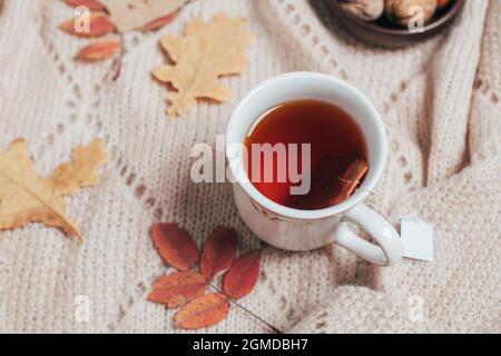 Tasse heißer Tee, Herbstblätter auf beigefarbenem, kuscheligem Karomuschel. Konzept für warme Getränke. Stockfoto