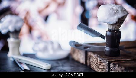 Rasierzubehör auf einem Hintergrund mit Holzstruktur. Werkzeuge. Einweg-Rasierer, Bürste, Rasierer mit Schaumgefahr. Stockfoto