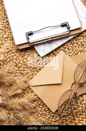Flatlay der Zwischenablage mit leerem Papierbogen. Tastatur, Pampas Gras, Schreibwaren auf beigem Strohhintergrund. Minimalistischer Schreibtisch im Home Office. Oben Stockfoto