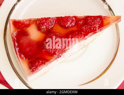 Köstliches Stück Erdbeerkäsekuchen auf einem weißen Teller, auf dem Tisch mit einer rot karierten Serviette, Draufsicht. Stockfoto