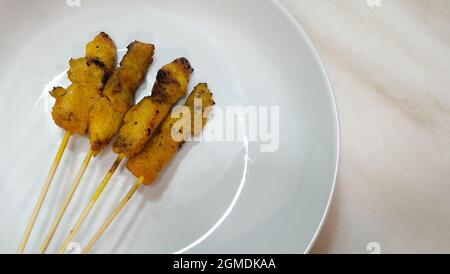 Vier Hähnchen-Satay auf einem weißen runden Teller serviert, auf einer Marmoroberfläche platziert. Stockfoto