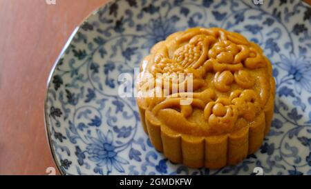 Nahaufnahme eines braunen Mondkuchens mit schönem Muster, auf einem blauen Teller platziert. Mooncake ist ein chinesisches Gebäck, das traditionell während der Mitte des Herbstes Fe gegessen wird Stockfoto