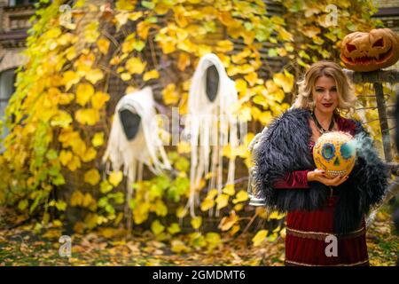 Schöne Frau im Hexenkostüm hält Kürbis im ack-o-Laternen Stil gemalt. Dampfender Kürbis im Dekor für Halloween. Zauberin auf dem Hintergrund von gh Stockfoto