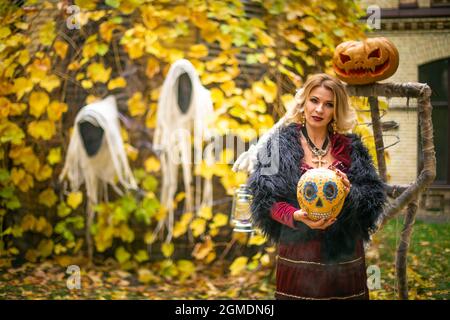 Schöne Frau im Hexenkostüm hält Kürbis im ack-o-Laternen Stil gemalt. Dampfender Kürbis im Dekor für Halloween. Zauberin auf dem Hintergrund von gh Stockfoto