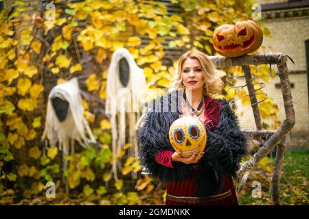 Schöne Frau im Hexenkostüm hält Kürbis im ack-o-Laternen Stil gemalt. Dampfender Kürbis im Dekor für Halloween. Zauberin auf dem Hintergrund von gh Stockfoto