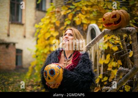 Schöne Frau im Hexenkostüm hält Kürbis im ack-o-Laternen Stil gemalt. Dampfender Kürbis im Dekor für Halloween. Zauberin auf dem Hintergrund von gh Stockfoto