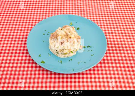 Teller mit russischem Salat mit Oliven mit Mayonnaise, gekochten Eiern und Thunfischkonserven mit Petersilie auf weißer und roter Tischdecke Stockfoto