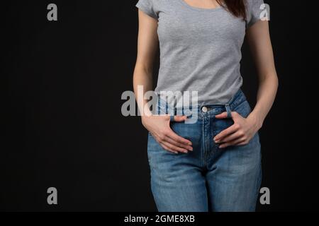 Schlanke junge Frau in klassischer blauer Jeans und legerem grauem Hemd im Studio. Nicht erkennbarer weiblicher Modellkörperteil mit Händen auf der Taille Stockfoto