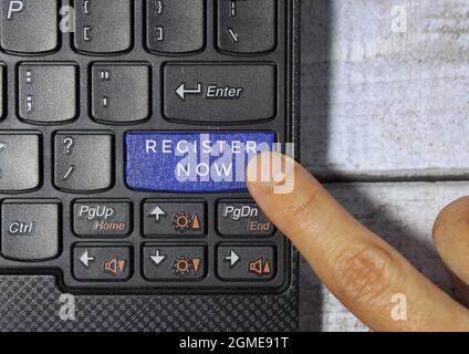 Fingerdruck auf eine blaue Taste mit der Bezeichnung JETZT REGISTRIEREN mit Symbol auf einem Computertastaturkonzept Stockfoto