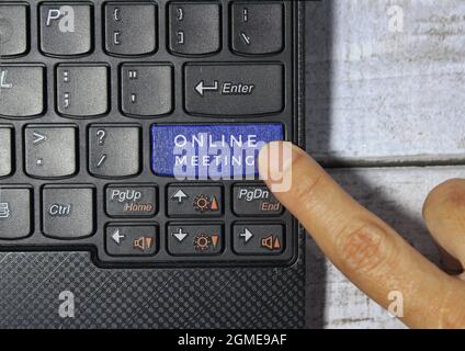 Fingerdruck auf eine blaue Taste mit der Bezeichnung ONLINE-MEETING mit Symbol auf einem Computertastaturkonzept Stockfoto