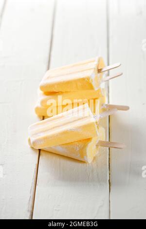 Hoher Stapel gelber Ananas-Eislollies auf einem Holztisch mit weiß gefliestem Hintergrund. Gefiltert für Retro-Effekt Stockfoto