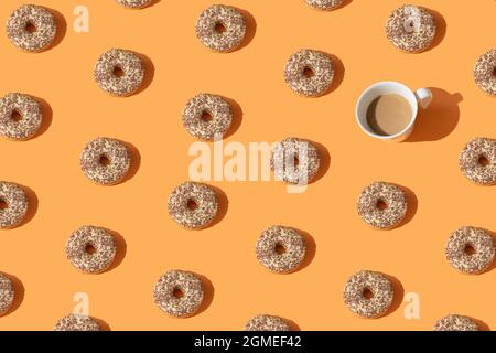 Donuts und eine weiße Tasse Kaffee auf orangefarbenem Hintergrund. Kreatives Muster Süßes Essen Konzept. Nachtisch. Süßes Gericht. Layout. Draufsicht. Flach liegend. Stockfoto