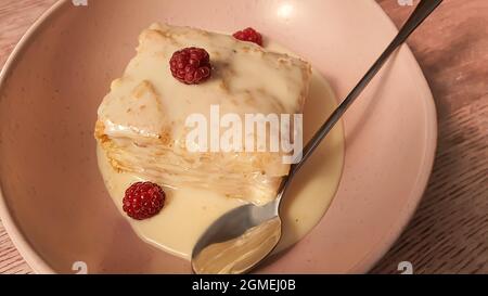 Dessert Napoleon mit Pudding, kondensierte Milchsauce, verziert mit Himbeeren. Auf einem natürlichen Hintergrund aus Holz. Speicherplatz kopieren Stockfoto